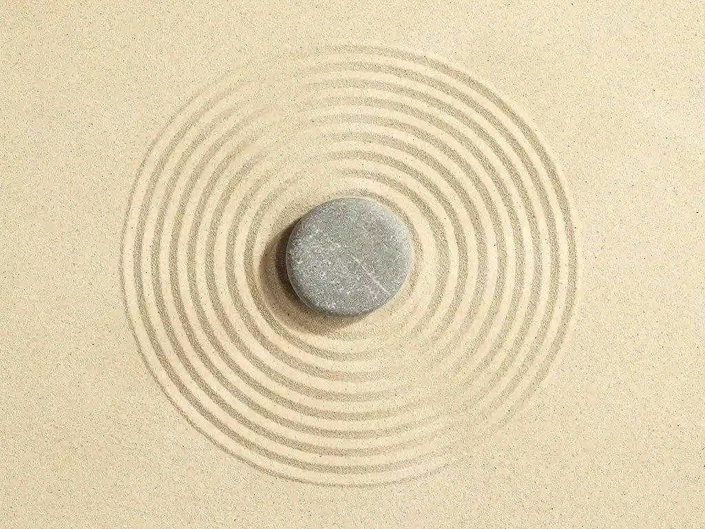 Gladde steen in geharkt zenzandtuin met concentrische cirkels, bovenaanzicht met minimalistisch design